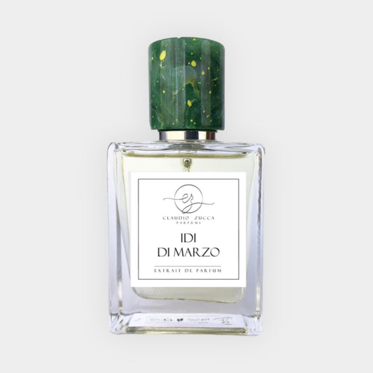 Een volle fles Claudio Zucca Idi Di Marzo met een elegante, transparante glazen verpakking en een groen, fleurig dopje. Het parfum wordt gepresenteerd als een extrait de parfum.