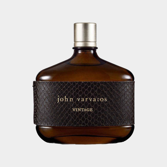 Een bruine glazen flacon met een leren label en john varvatos VINTAGE erop gedrukt, die het geurmonster van John Varvatos Vintage vertegenwoordigt. De flacon heeft een elegante, tijdloze uitstraling.