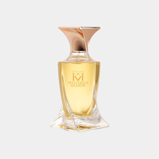 Een elegant parfumflesje van Karakash met de naam Mysterious Shadow, gekenmerkt door een unieke vorm en een gouden dop. De vloeistof heeft een warme, amberkleurige tint.