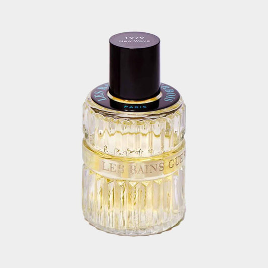 Een transparante geurflacon van Les Bains Guerbois New Wave 1979, versierd met een gouden band en een zwarte dop, die het luxe en retro ontwerp van de parfum benadrukt.