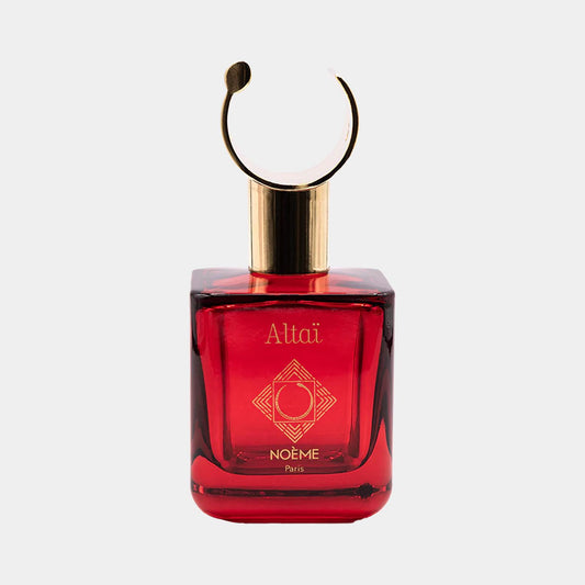 Een luxe parfumfles van Noème Paris met de naam Altaï, gekenmerkt door zijn opvallende rode kleur en elegante gouden details. De unieke dop in cirkelvorm voegt een artistiek accent toe aan het ontwerp.