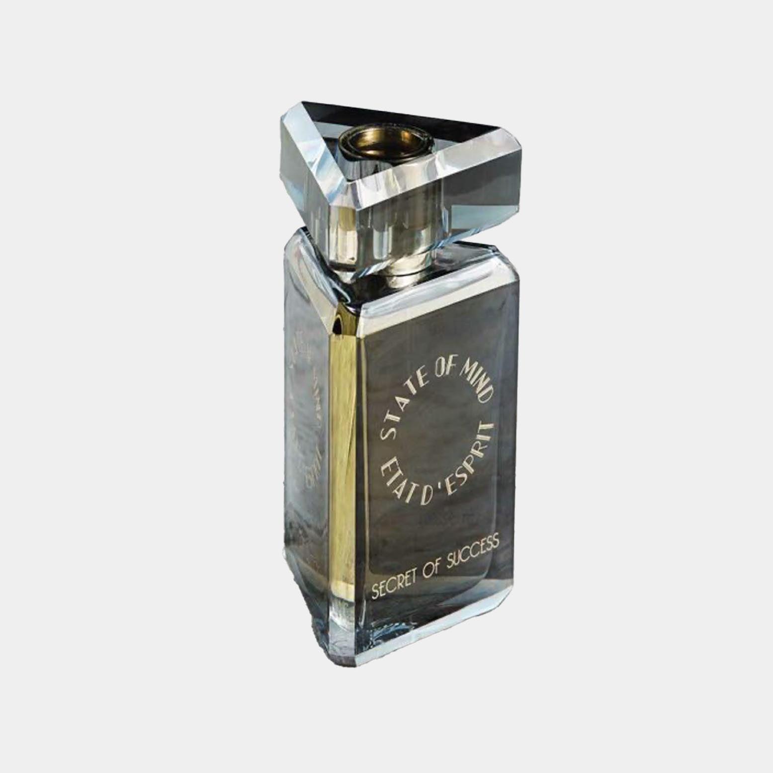 State of Mind Secret of Success is een luxe parfumfles met een unieke, driehoekige dop en elegante vormgeving, die staan voor zelfvertrouwen en succes. De fles is versierd met de naam van het merk en het parfum.
