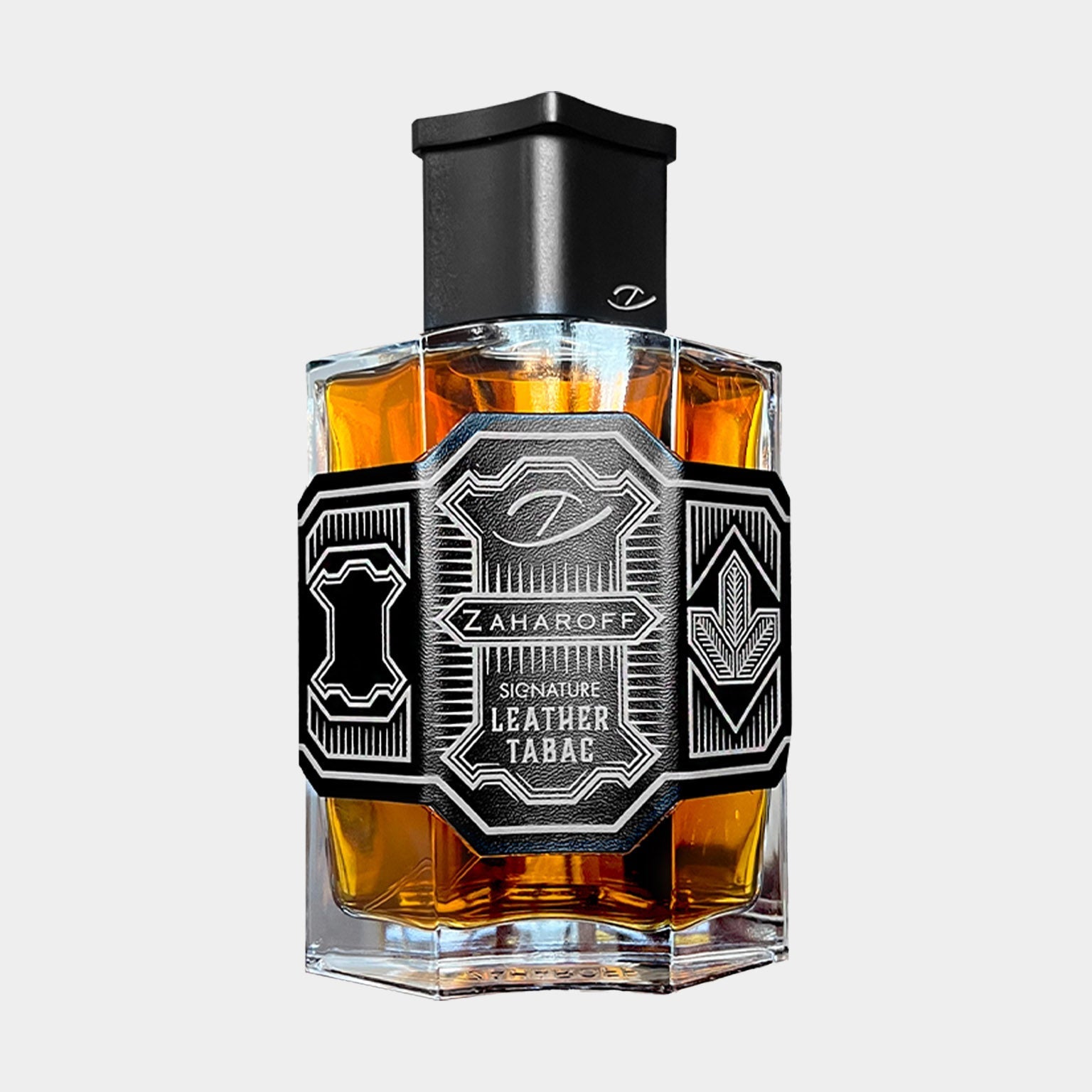 A clear bottle of Zaharoff Signature Leather Tabac, featuring an elegant black label with intricate designs, showcasing a warm amber liquid inside. The bottle has a distinctive geometric shape and a sleek black cap.