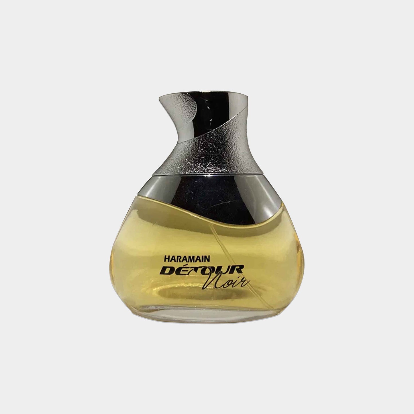Al Haramain Détour Noir Sample is a stylish, curved glass fragrance bottle showcasing a warm, amber liquid. The sleek design is accentuated by a metallic silver cap, reflecting elegance and sophistication.